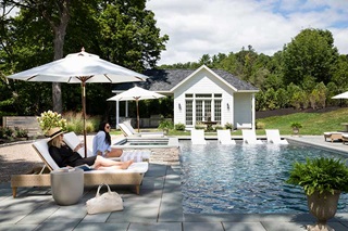 Two women sitting on lounge chairs next to a pool under umbrellas.