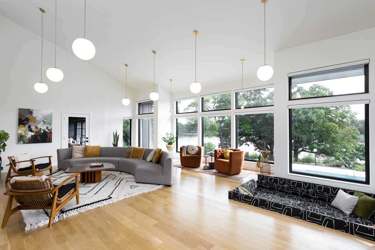 A modern living room with curved gray couch featuring Marvin Essential Casement Picture windows.