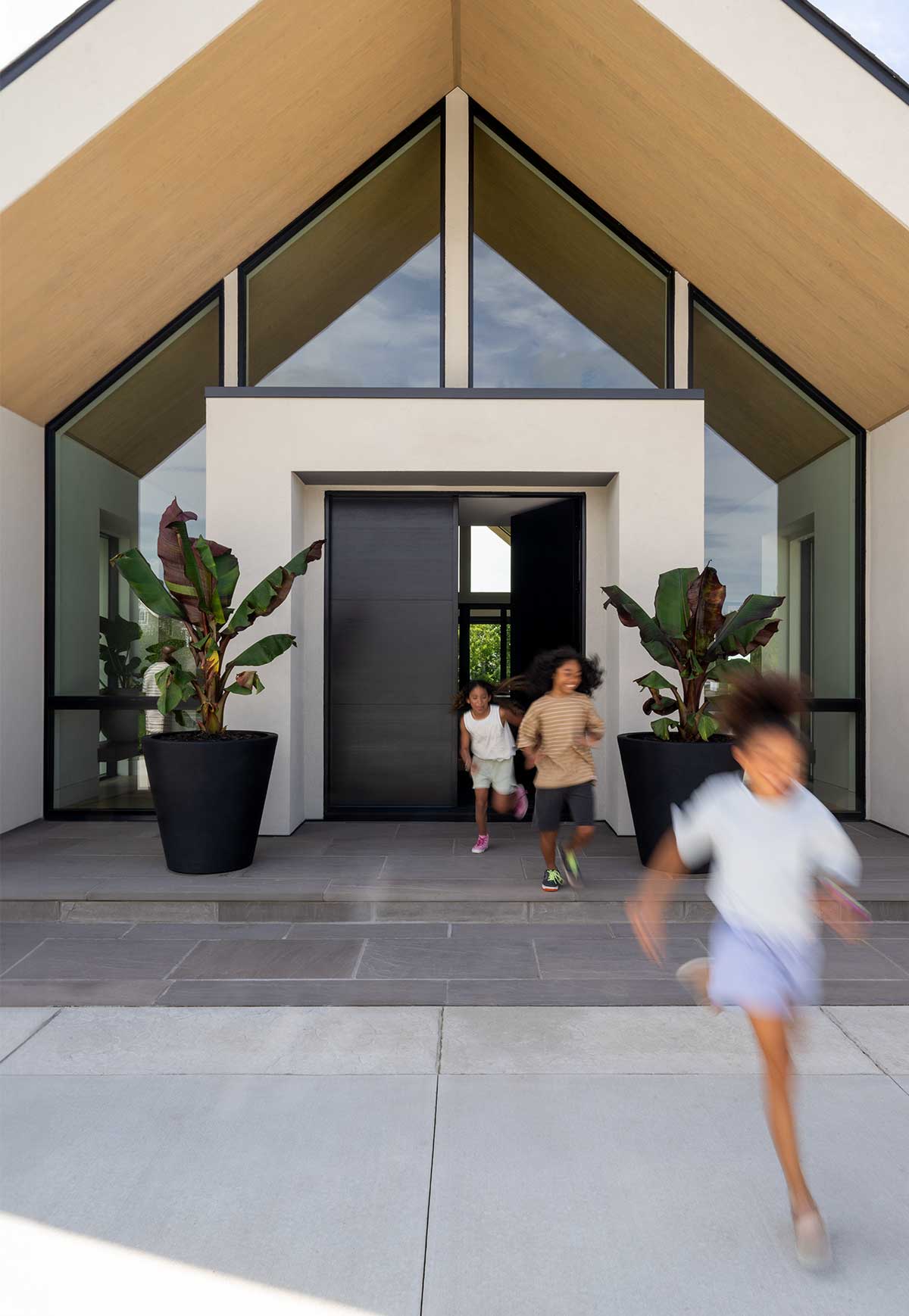 Three children running out the front door of a modern home featuring Marvin Ultimate Specialty Shape windows and doors.