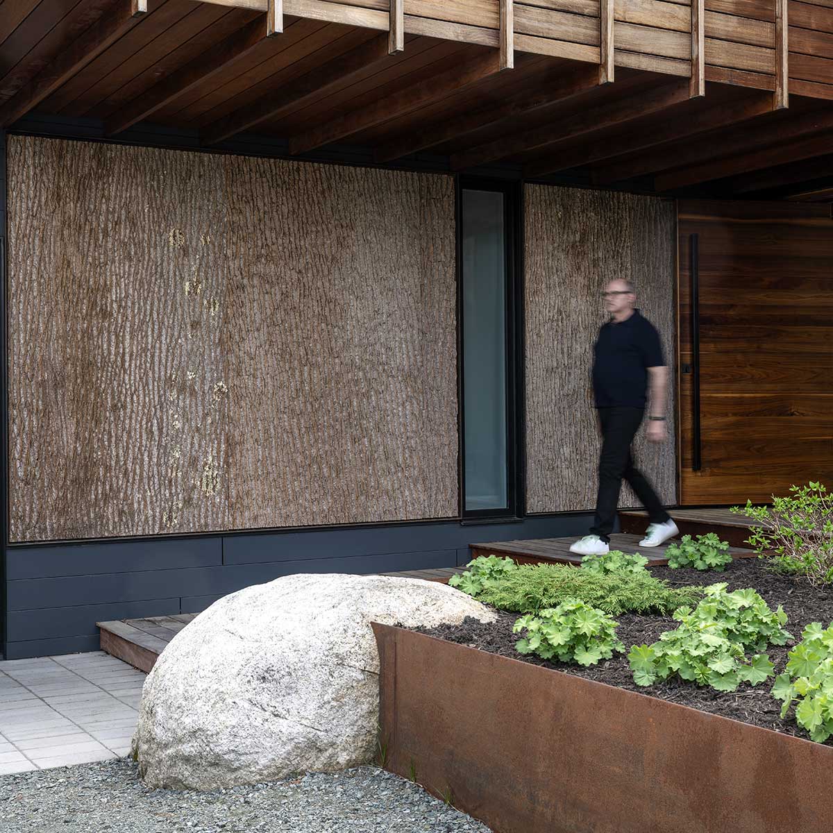 A person walking next to a modern home in New Hampshire, featuring Marvin Modern windows and doors.