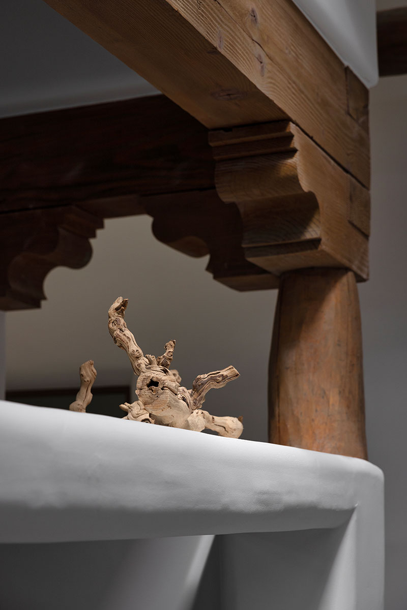 A close-up of wood corbels on the interior of a Pueblo-style home in Santa Fe, New Mexico, near a piece of driftwood on a white stone surface.