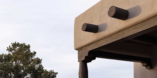 A close-up on the exterior of a Pueblo-style home in Santa Fe, New Mexico, showing bullnose edges and wood corbels near the roof.