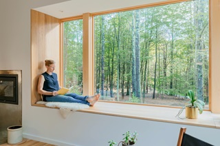 A woman reading on a window seat, featuring Marvin Signature Ultimate picture and corner windows.