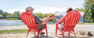 Two people sitting in lawn chairs with beverages looking out onto a lake